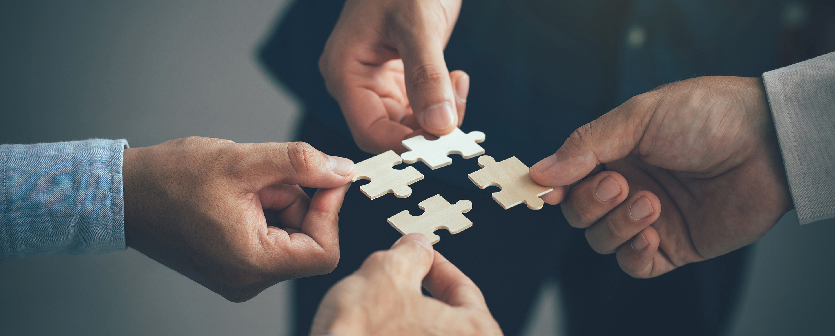 Vier Hände reichen sich Puzzelteile